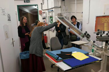 Five people are being shown the screen printing machine.